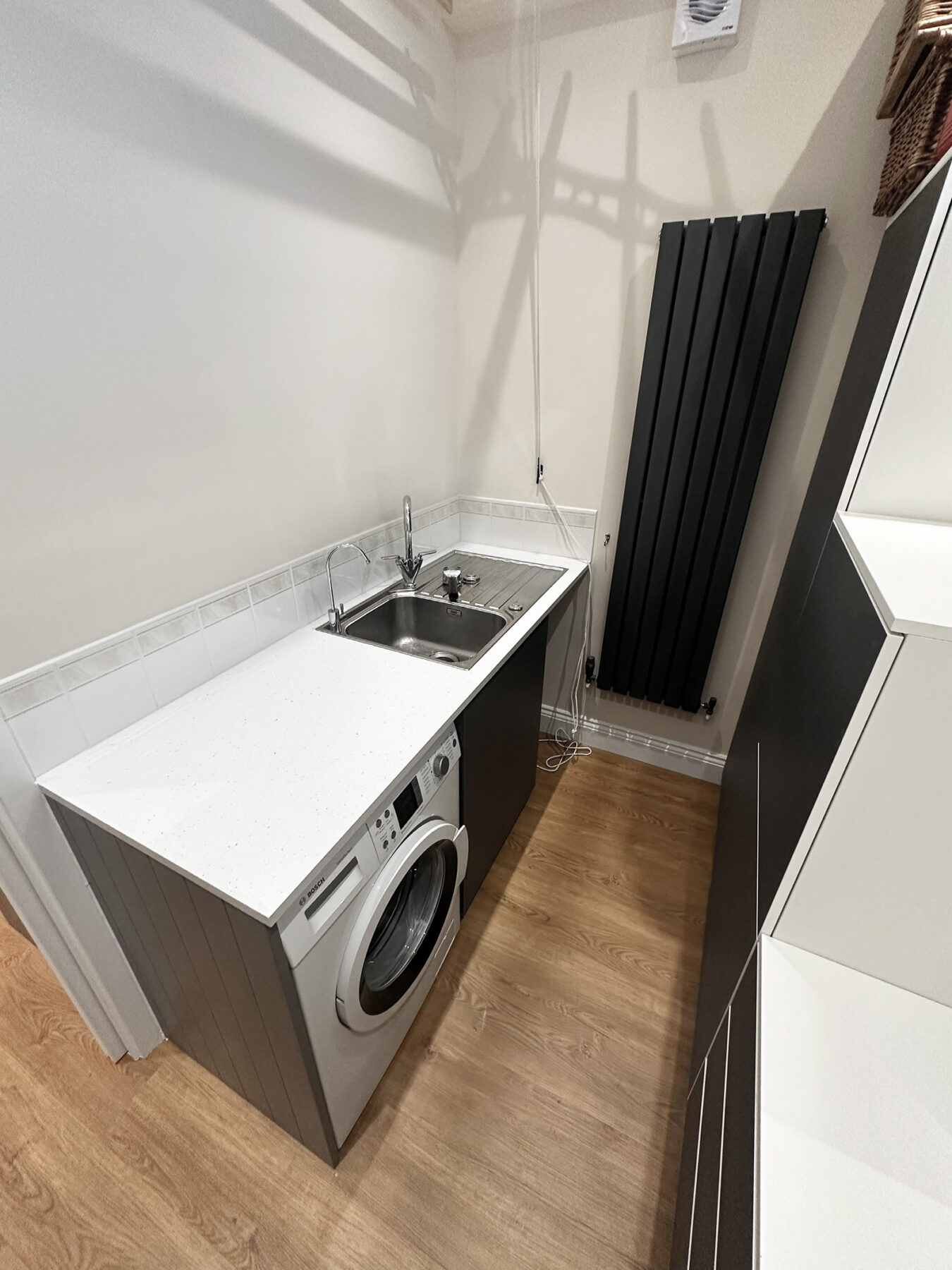 Utility room with white worktop, fitted storage, washing machine and black radiator in Holland Park