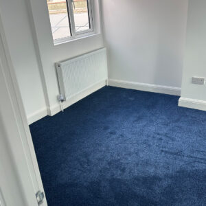 Completed loft bedroom with deep blue carpet, window and radiator in Southwark