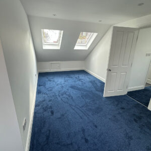 Spacious completed loft bedroom with two VELUX windows and blue carpet in Southwark