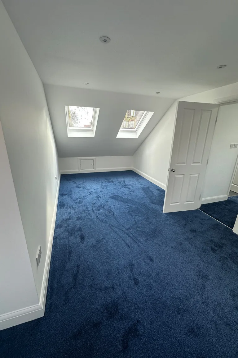Spacious completed loft bedroom with two VELUX windows and blue carpet in Southwark