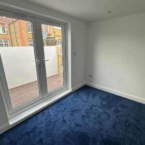 Completed loft bedroom with blue carpet and glazed doors overlooking the roof terrace in Southwark