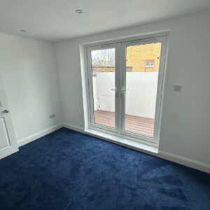 Completed loft bedroom with blue carpet and double doors opening onto the roof terrace in Southwark
