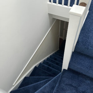 Completed loft staircase with deep blue carpet, white balustrade and timber handrail in Southwark